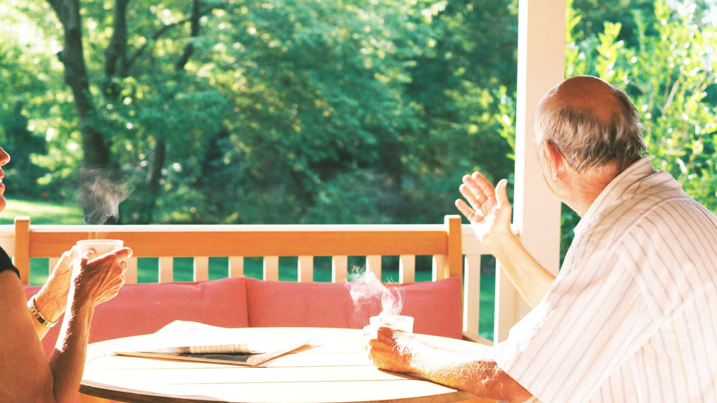 A retired couple enjoying coffee together on their porch on a sunny morning