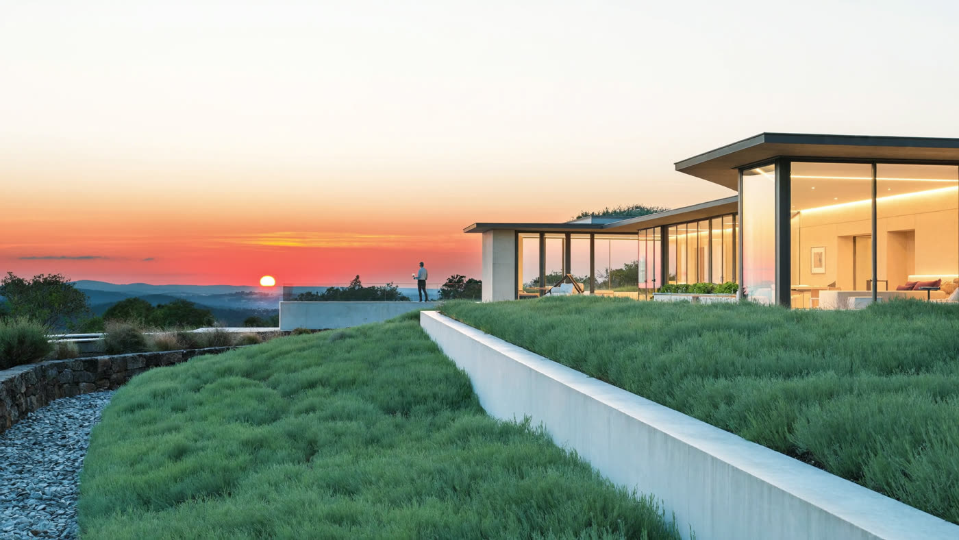 An elegant hillside home glowing warmly at sunset with terraced gardens