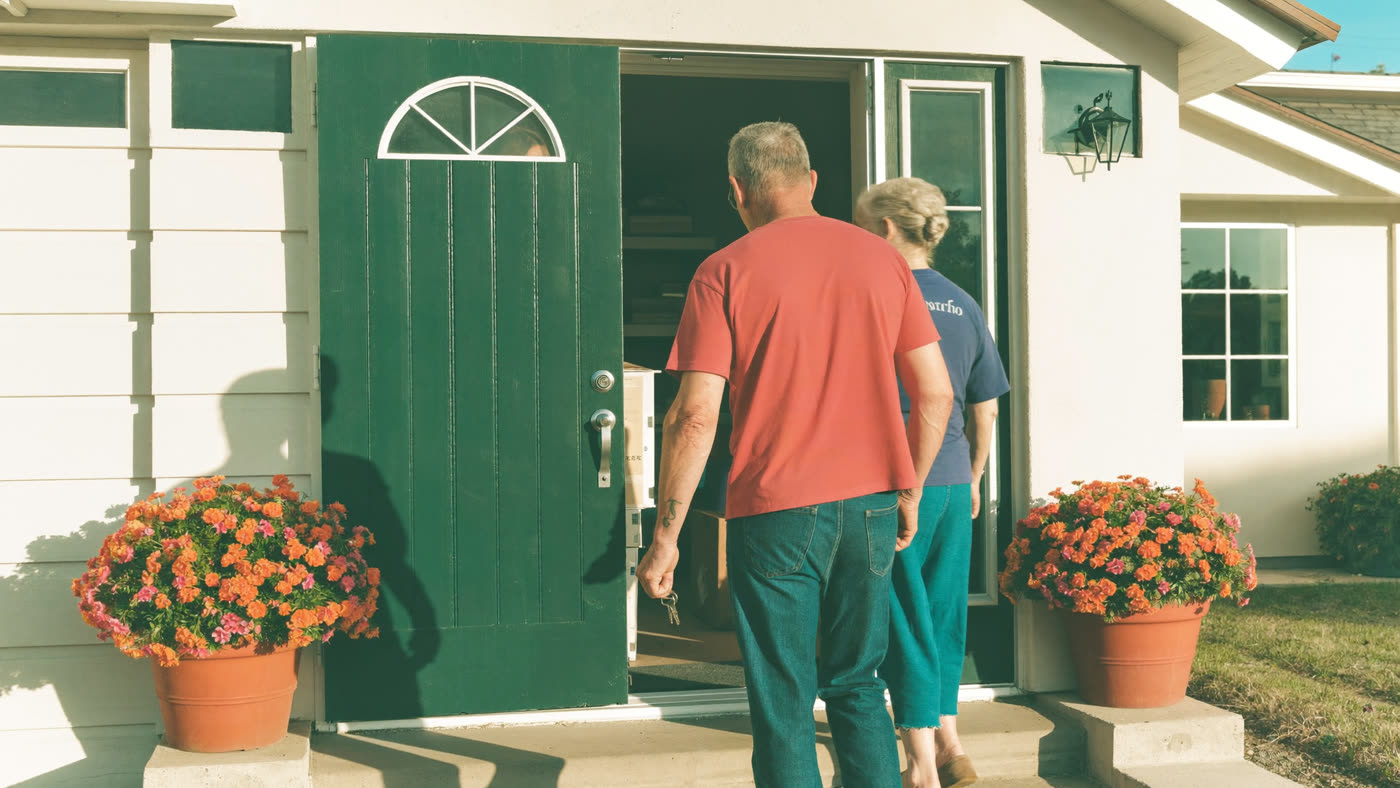 A couple stepping through the front door of their new single-story home, keys in hand