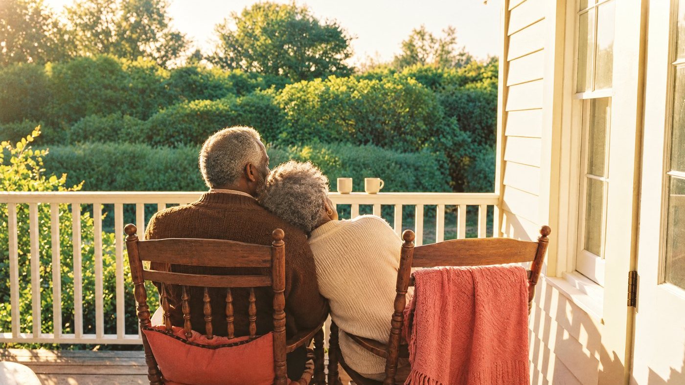 A couple sitting close together on their porch at golden hour, looking out at the garden